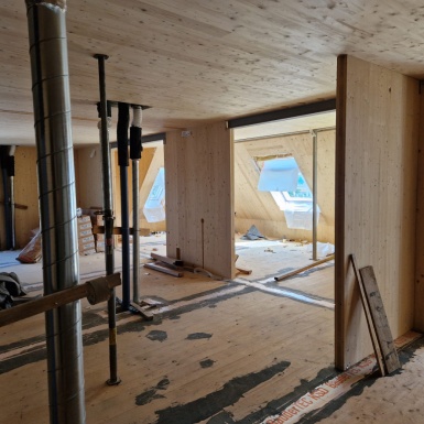 Wände aus Holz mit Fensterausschnitten, Holzböden und Decke, Rohre im Dachgeschoss