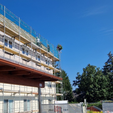 Wohnhaus Seitenansicht eingerüstet mit Tannenbäumchen und Arbeitern am Dachgeschoss