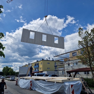 Fertigwand mit Fensterausschnitten wird von Kran aufs Dach gehoben