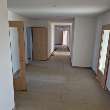 Weißer Gangbereich mit beigen Fliesenboden und hier führen rechts und links hellbraune Türen teilweise mit Glas in die Räume