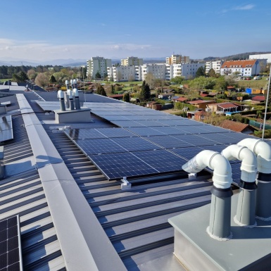 Graues Dach mit Photovoltaikanlage und Blick auf Häuser, Gärten und den Himmel