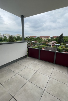 Ausblick von der Terrasse mit grauem Fliesenboden und Überdachung im Obergeschoss auf Gärten Häuser und den Himmel