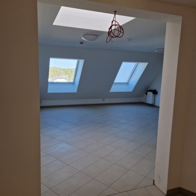 Raum weiß ausgemalt mit beigen Fliesen und 2 Dachschräge Fenster und einem herunterhängendem Kabel