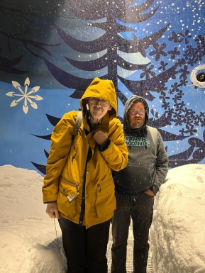 Zwei Männer mit Brille winterlich gekleidet stehen in einer künstlichen Winterlandschaft