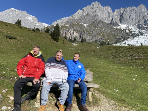 Drei Männer sitzend auf einer Bank in einer Wiesen und Berglandschaft