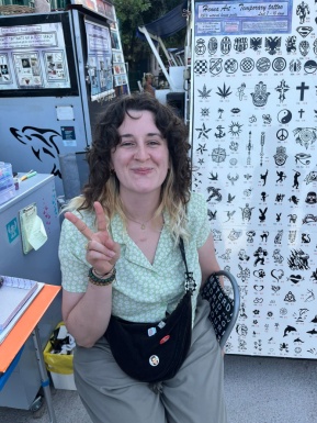 Frau sitzt bei Stand mit Henna Tattoos und zeigt zwei Finger hoch