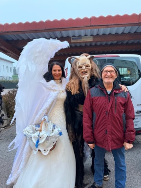 Mann mit Personen die als Engel und Krampus verkleidet sind