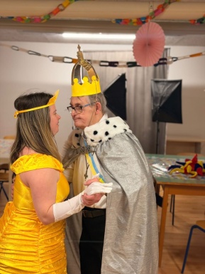 Frau mit gelbem Kleid tanzt mit Mann mit Krone und Umhang