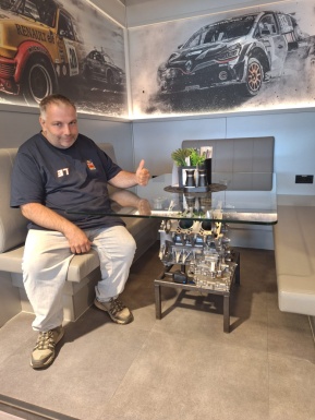Mann sitzt bei einem Tisch dahinter Bilder von Rennautos