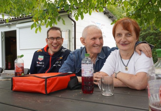 Zwei Männer und eine Frau sitzen beim Tisch im Freien