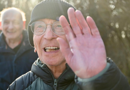 Mann winkt fr&ouml;hlich in die Kamera