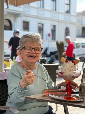 Frau sitzt im Au&szlig;enbereich eines Kaffeehauses vor einem gro&szlig;en Eisbecher