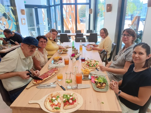 Gruppenbild beim gedeckten Mittagstisch mit Pizzen und Getr&auml;nken