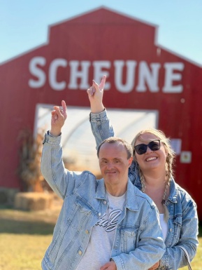 Ein Mann und eine Frau halten die Hand hoch und zeigen auf eine Scheune