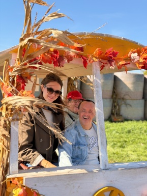 Betreuerin mit einer Bewohnerin und einem Bewohner in einem herbstlich dekorierten Wagen