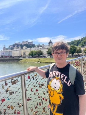 Frau mit Brille hält sich am Brückengelände wo Liebesschlösse befestigt sind fest, Wasser und Stadt im Hintergrund