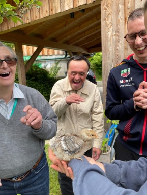 Vier Personen im Garten, eine hält ein Küken, die anderen lachen erfreut