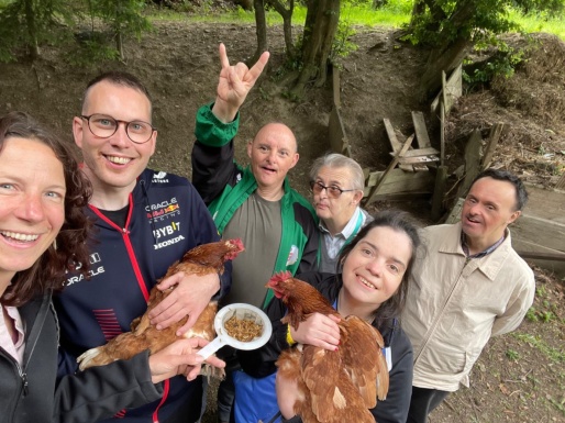 Zwei Frauen und vier Männer lachen in die Kamera, zwei von ihnen halten ein Huhn