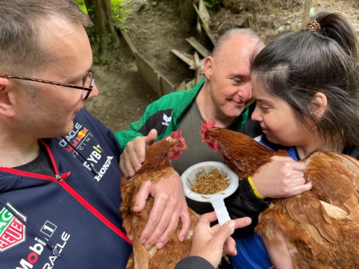 Zwei Männer und eine Frau halten ein Huhn in der Hand, streicheln und füttern es
