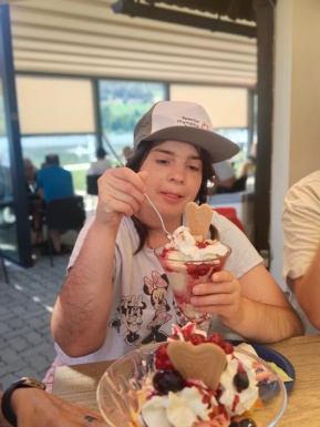 Frau mit Kappe sitzt vor einem großen Becher Eis und beginnt zu essen