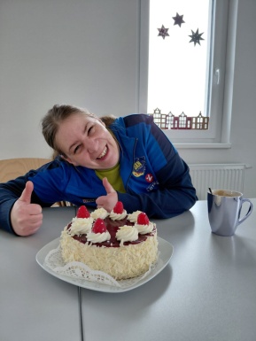 Frau mit Torte und Kaffee zeigt beide Daumen hoch und l&auml;chelt