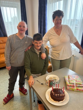 Ein Mann und eine Frau stehen neben einem sitzenden Mann der Geburtstag feiert