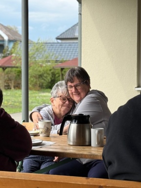 Zwei Frauen die sich freundschaftlich umarmen bei Tisch auf der Terrasse