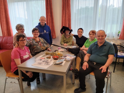 Menschen sitzen bei Tisch mit Kräuter, Hexenbesen und Hut