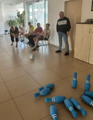 Personen sitzen und schauen einer Frau zu die eine Bowlingkugel rollt