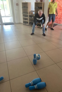 Mann rollt eine Bowlingkugel durch den Gang und wirft einen Kegel um