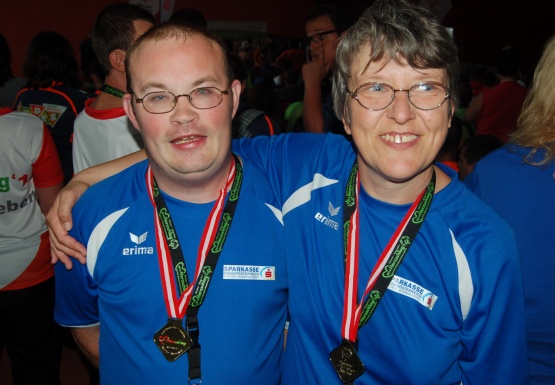 Mann mit Brille und Frau mit Brille mit Medaille umarmen sich und lächeln
