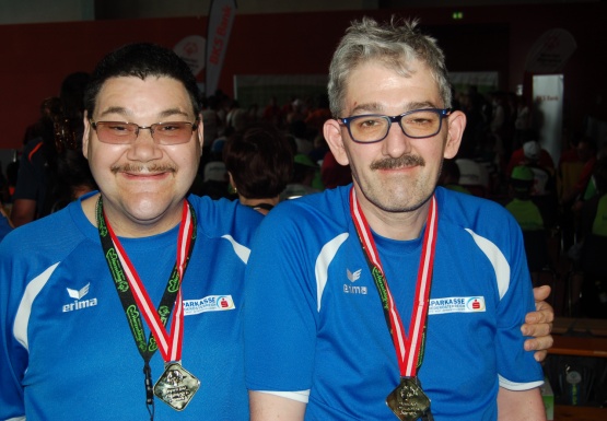 Zwei Männer mit Brille und Medaille umarmen sich und grinsen