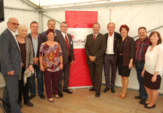 Gruppenfoto mit Damen und Herren schön gekleidet vor DomiZiel Logo