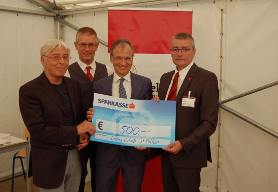 Vier Männer im Anzug mit einem Spendenscheck im Wert von 500 Euro hochhaltend