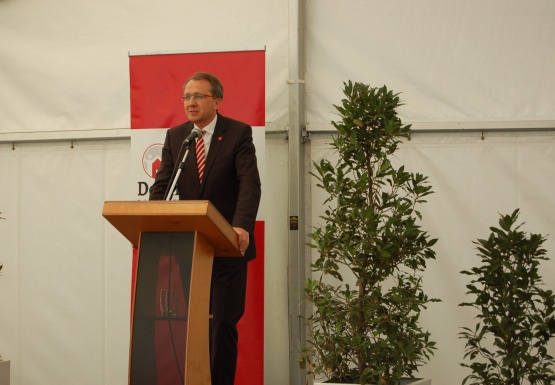 Ein Mann mit Anzug steht vor einem Podium mit Mikrofon und hält eine Ansprache