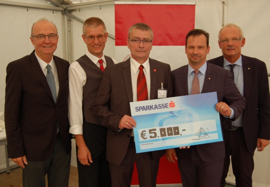 Fünf Männer im Anzug mit einem Spendenscheck im Wert von 5.000 Euro hochhaltend