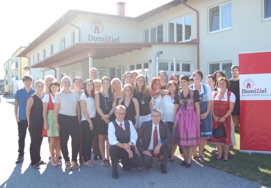 Menschengruppe bei Sonnenschein schön gekleidet vor dem Wohnhaus DomiZiel