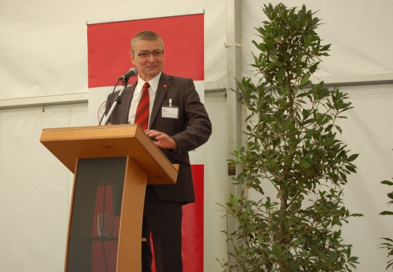 Ein Mann im Anzug lächelnd vor einem Podium mit Mikrofon stehend