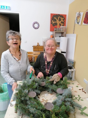 Zwei Frauen lächelnd beim Dekorieren eines Adventkranzes der auf einem Tisch liegt