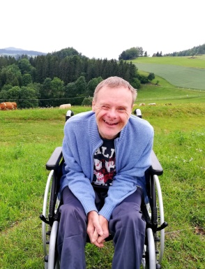 Mann lachend in einem Rollstuhl auf einer grünen Wiese