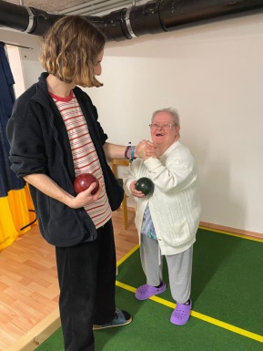 Mann hält die Hand einer kleinen Frau mit Brille und beide haben eine Bocciakugel in der Hand