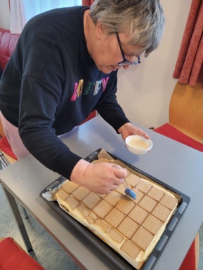 Frau bestreicht Blechkuchen bedeckt mit Keksen mit Flüssigkeit