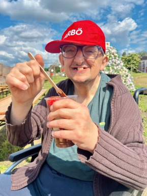 Ein Mann im Rollstuhl, mit roter Kappe genießt Erdbeeren mit Schokosauce