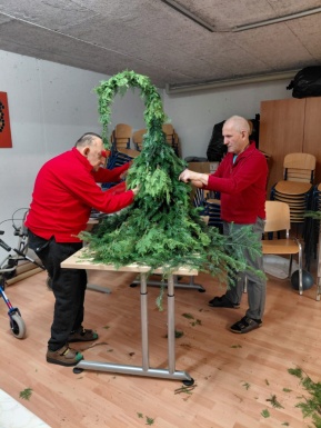 Zwei Männer basteln einen Wichtel aus Tannenzweigen