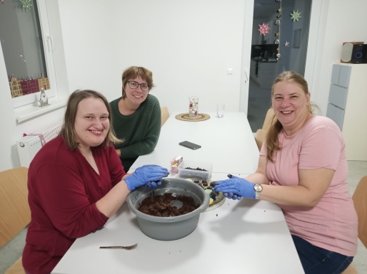 Drei Frauen sitzen beim Tisch und formen Kekse