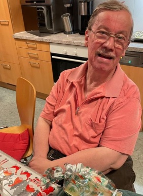 Mann mit Brille sitzt beim Tisch mit Geschenken